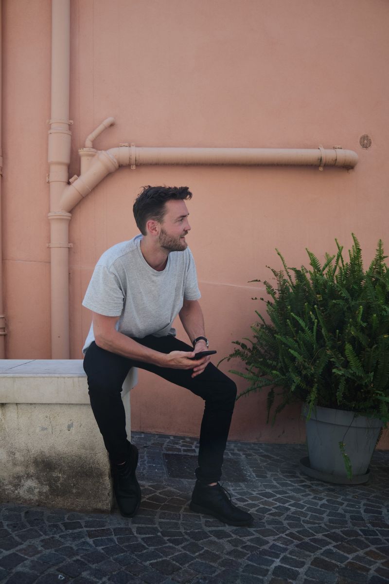 Robin souriant, assis devant un mur rose parcouru de canalisations